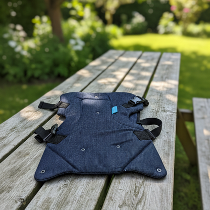 Blue baby carrier on a wooden bench outdoors with greenery in the background