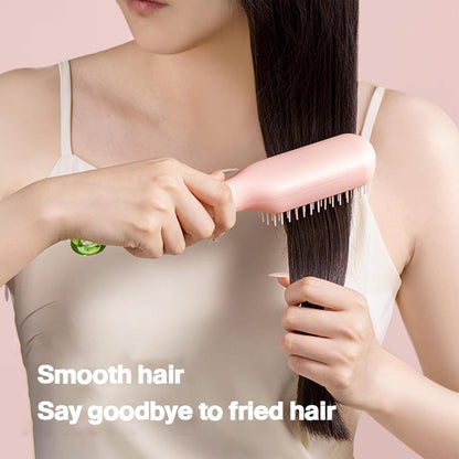 Person using a hair straightening brush on their hair with a pink background